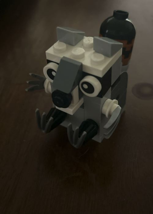 A small grey-and-white brick-built raccoon photographed from the front on a dark table